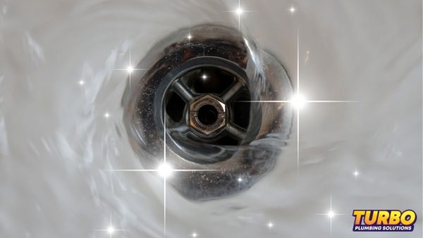 Close-up of a clean, shiny sink drain with sparkling effects, highlighting expert drain maintenance; Turbo Plumbing Solutions logo appears in the bottom right corner.