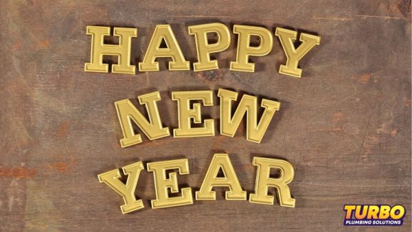 Gold block letters spell out “HAPPY NEW YEAR” on a wooden surface, with a small Turbo Plumbing Solutions logo in the bottom right corner—a festive scene perfect for Brisbane homeowners seeking New Year tips for their home plan.