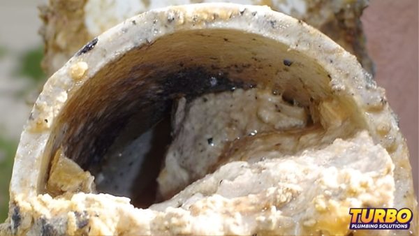 Close-up of a severely clogged pipe with heavy buildup and residue inside, highlighting restricted water flow. TURBO Plumbing Solutions logo is visible in the bottom right corner, emphasizing the importance of drain protection to prevent fatbergs.