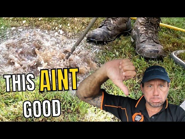 A man gives a thumbs-down sign next to muddy water around a pair of boots on a grassy area. The text "THIS AIN'T GOOD" is overlayed on the image.