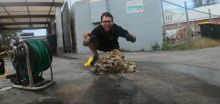 A person wearing gloves squats beside a heap of gunk in an outdoor area next to a wall, with some cleaning equipment and hose visible in the foreground, pondering if flushable wipes are bad for the environment.