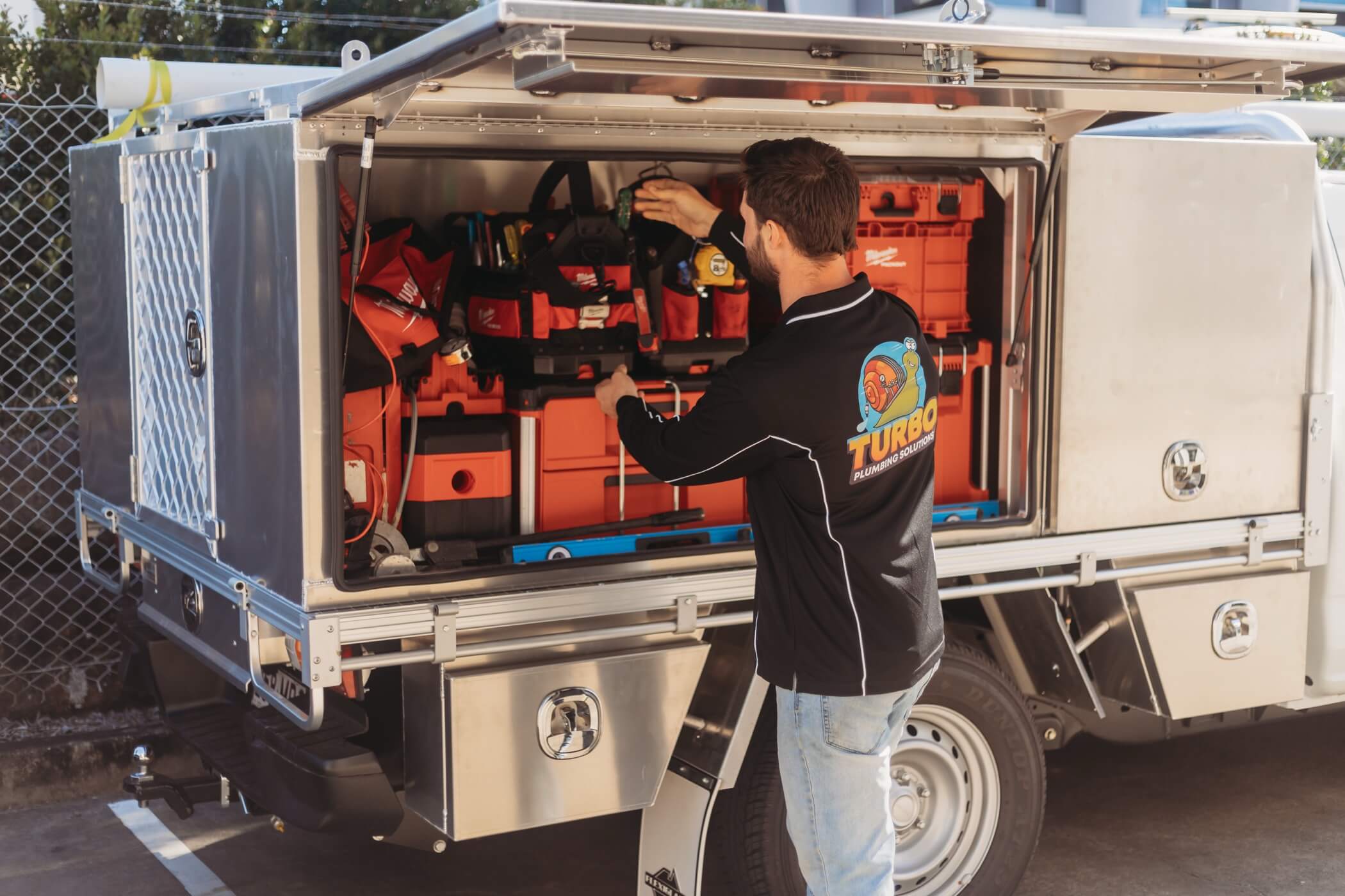 A man in a Turbo-branded shirt organizes equipment inside the open side compartment of a utility vehicle parked outdoors.