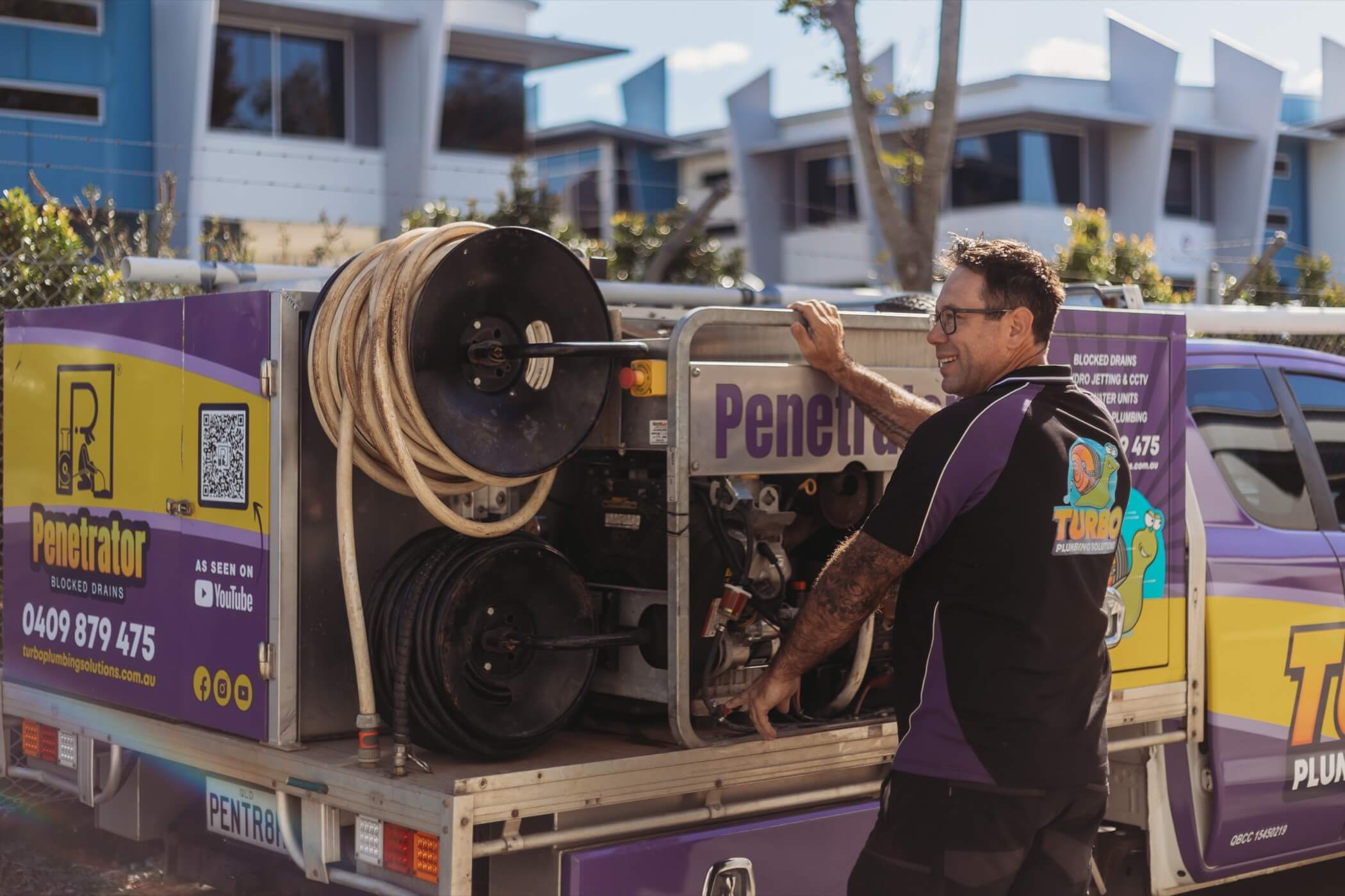 A plumber stands beside a service vehicle equipped with hoses and plumbing equipment, branded with "Penetrator" and contact details.