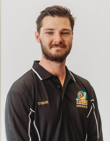 A man with short brown hair and a beard, wearing a black "Turbo Plumbing & Roofing" polo shirt with the name "Tyson" embroidered on it, stands against a plain white background.