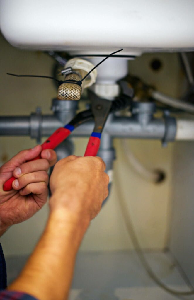 A person is using a wrench to tighten a pipe under the sink, ensuring proper drain repairs to prevent any potential blockages.