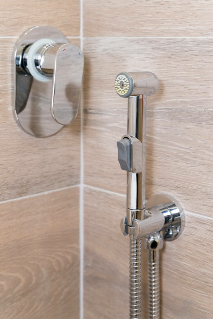 Close-up of a modern shower fixture in a bathroom, featuring a handheld showerhead and a mounted control lever, against a tiled wall. This impeccable setup ensures you won’t need blocked drain repairs anytime soon.