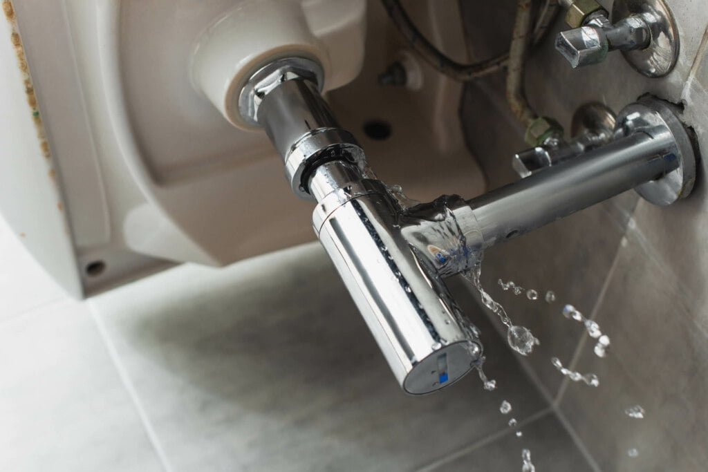 A close-up of a plumbing fixture leaking water onto a tiled floor, with water droplets visible on the chrome surface. This scene highlights the need for immediate blocked drain repairs to prevent further damage.